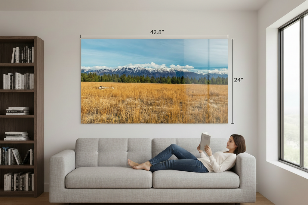 Woman lying on a couch reading a tablet in a living room with a large acrylic photograph displaying a scenic landscape.